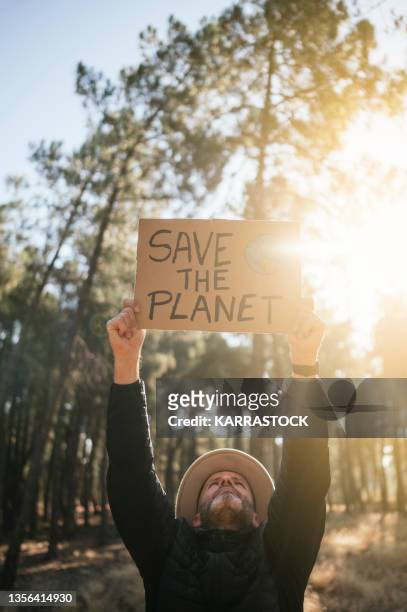 man in the woods holding a cardboard sign that says save the planet - exigir - fotografias e filmes do acervo