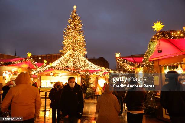 People, many wearing protective face masks, walk past Christmas market stalls near the Cologne Cathedral during the fourth wave of the coronavirus...