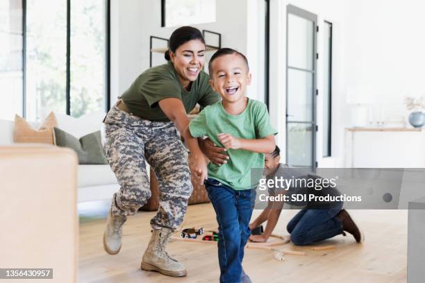 después del trabajo, una mujer soldado persigue a su hijo en la casa - war veteran fotografías e imágenes de stock