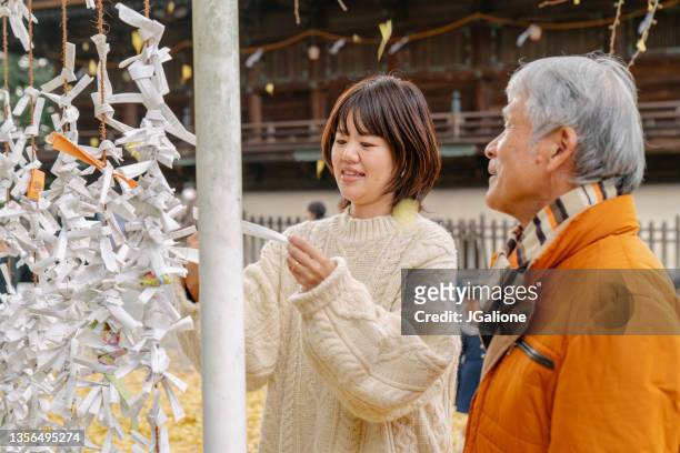 père aîné et fille adulte liant la fortune du nouvel an dans un temple japonais - buddhist new year photos et images de collection