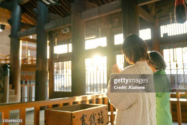 senior woman and her daughter praying at a japanese temple for hatsumode - shinto shrine stock pictures, royalty-free photos & images