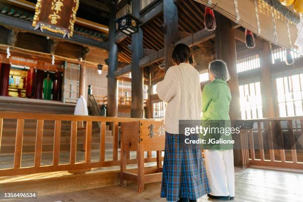 senior woman and her daughter praying at a japanese temple for hatsumode - shrine stock pictures, royalty-free photos & images