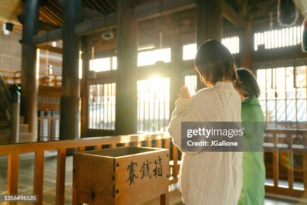 senior woman and her daughter praying at a japanese temple for hatsumode - shinto stock pictures, royalty-free photos & images