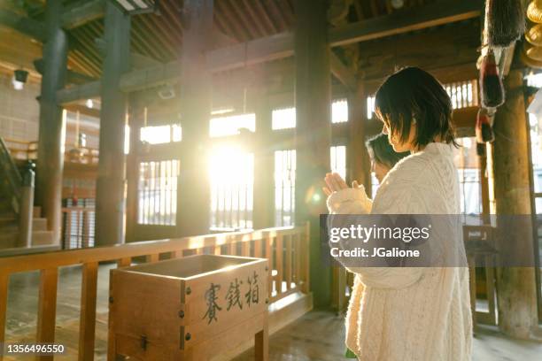 senior woman and her daughter praying at a japanese temple for hatsumode - schrijn stockfoto's en -beelden