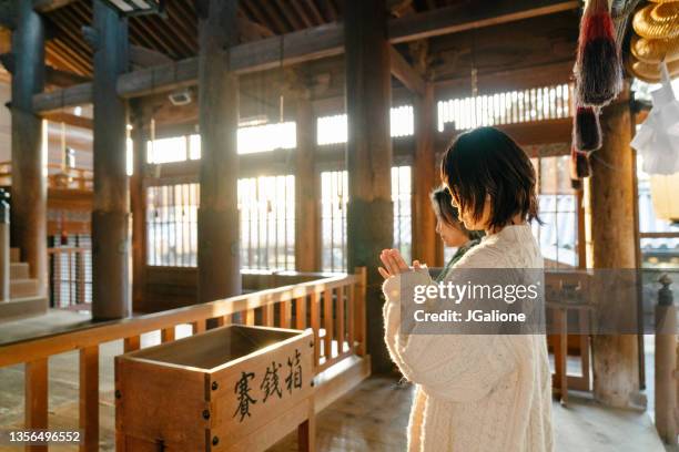 mujer mayor y su hija orando en un templo japonés por hatsumode - shrine fotografías e imágenes de stock