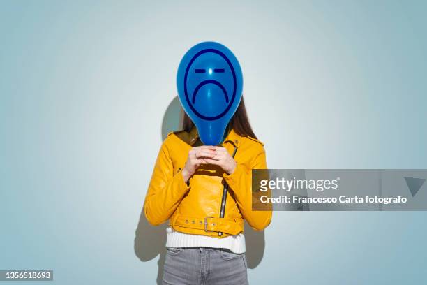 woman covering face with blue balloon with - sad face stock-fotos und bilder
