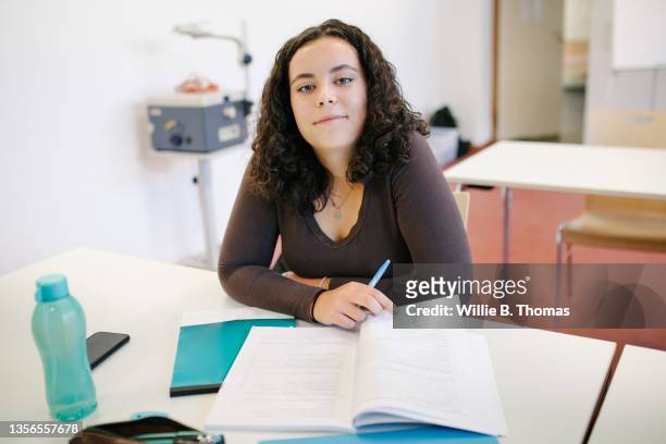 portrait of high school student sitting at desk with work book - alleen tienermeisjes stockfoto's en -beelden