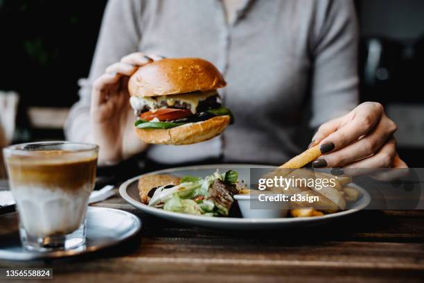 cropped shot, mid-section of young asian woman eating freshly made delicious cheeseburger, dipping fries in ketchup in a cafe. enjoying her lunch! lifestyle, people and food concept - hamburger foto e immagini stock