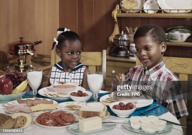 Boy and a girl eat a soup at a full table, circa 1960.