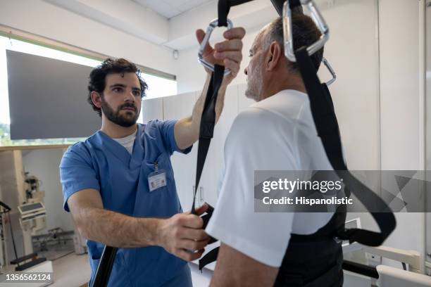 physical therapist helping a man get into a powered exoskeleton - powered exoskeleton stock pictures, royalty-free photos & images