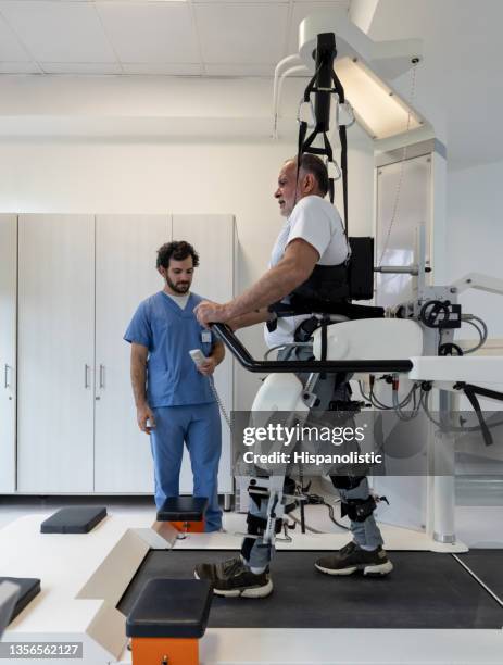 senior man walking with an exoskeleton while doing physiotherapy - afkickcentrum stockfoto's en -beelden