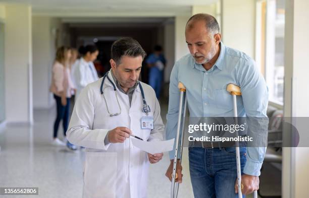 man using crutches while talking to a doctor at the hospital - man crutches stock pictures, royalty-free photos & images