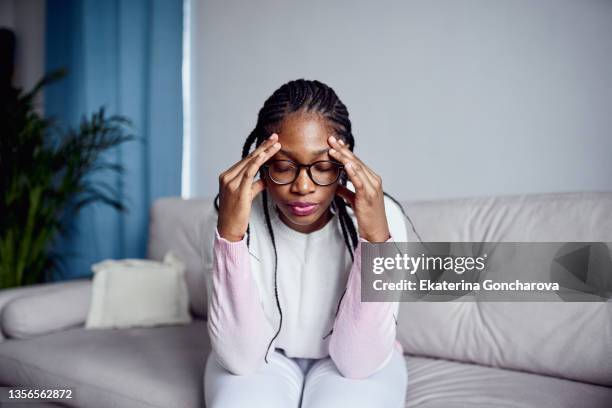 a young girl is sitting on the couch at home with her head in her hands. - tired person foto e immagini stock