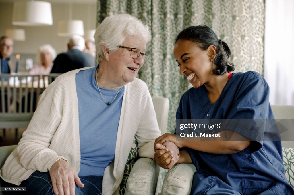 Cheerful female nurse holding hand of senior woman sitting at retirement home