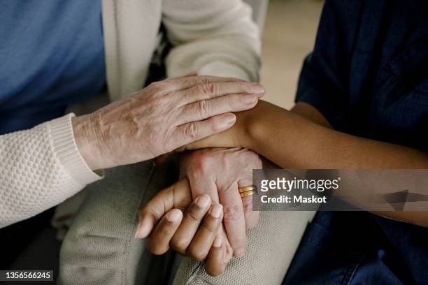 midsection of senior woman and female healthcare worker with hands stacked at retirement home - nursing homes ストックフォトと画像