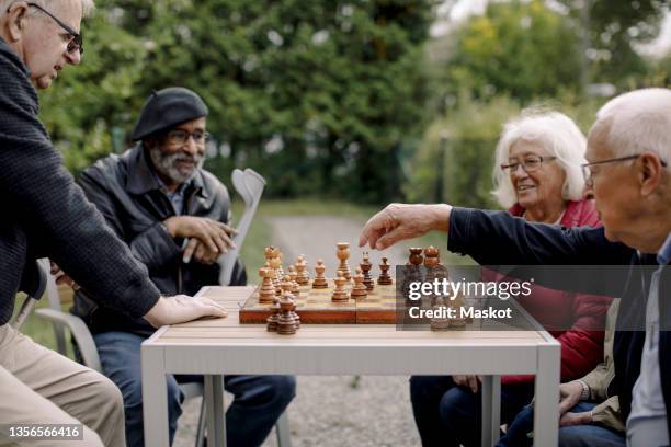 elderly man playing chess with male and female friends at park - chess fotografías e imágenes de stock