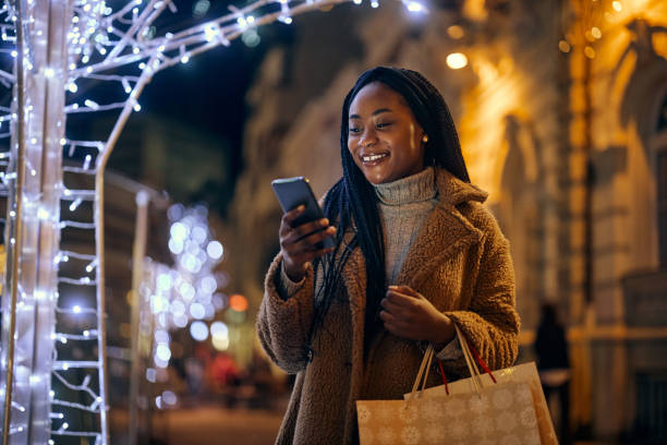 afro woman holding shopping bags and looking at her phone - black person using phone celebrating stock pictures, royalty-free photos & images