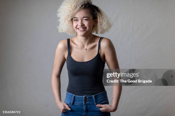 young woman laughing in front of grey background with hands in pockets - skinny blonde pics stock pictures, royalty-free photos & images