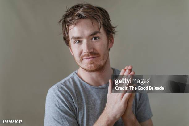 young man looking at camera with hands together against gray background - se frotter les mains photos et images de collection