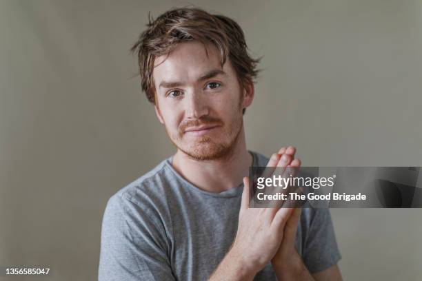 young man looking at camera with hands together against gray background - rubbing hands together stock pictures, royalty-free photos & images