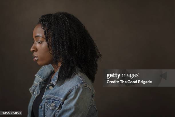 sideview of sad young woman wearing denim jacket in studio - sadness woman stock pictures, royalty-free photos & images