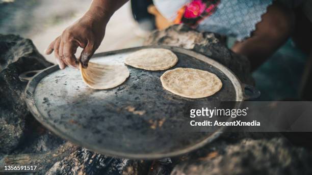 detail of woman preparing fresh tortillas on an open fire - haardvuur stockfoto's en -beelden