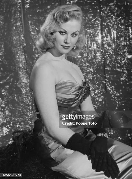English glamour model and actress Sabrina wearing an off-the-shoulder dress and evening gloves, circa 1955.