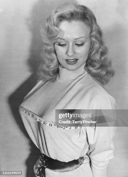 English glamour model and actress Sabrina , using a tape measure to measure her chest size, 2nd February 1957. She has recently insured her bust for...