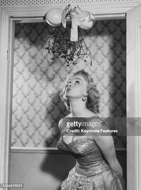 English glamour model and actress Sabrina waiting under a sprig of misteltoe, circa 1955.