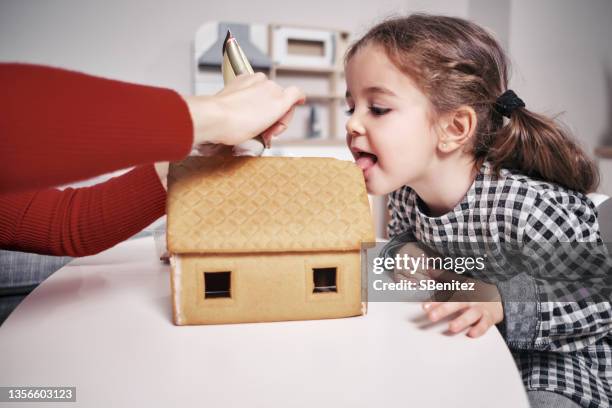 a girl is sucking on a gingerbread house before finishing it - gingerbread house stock pictures, royalty-free photos & images