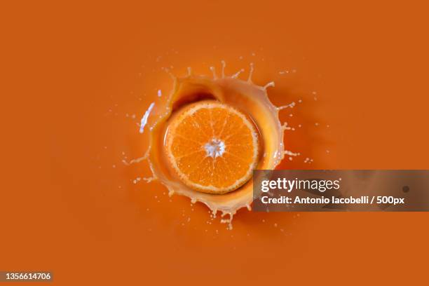 here come the sun,close-up of orange splashing in glass against orange background,bari,italy - splash jus d'orange stockfoto's en -beelden