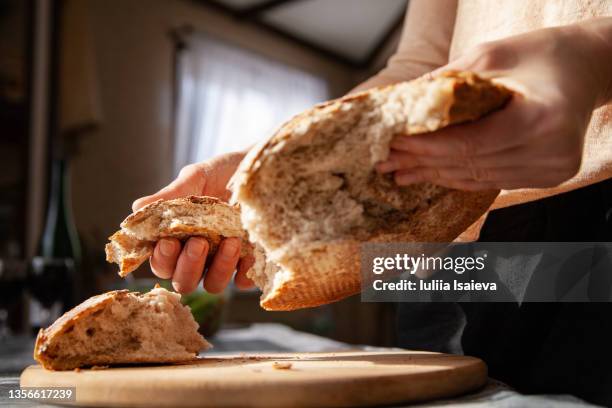 woman breaking rye bread above cutting board - roggebrood stockfoto's en -beelden