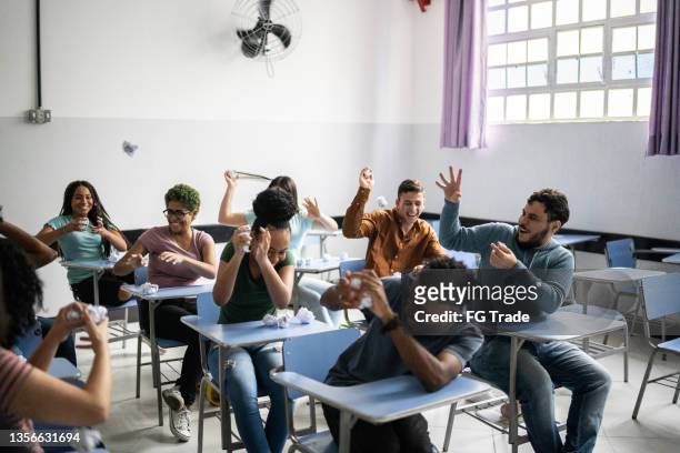 teenager-schüler, die sich im klassenzimmer gegenseitig mit papierkugeln bewerfen - classroom riot stock-fotos und bilder