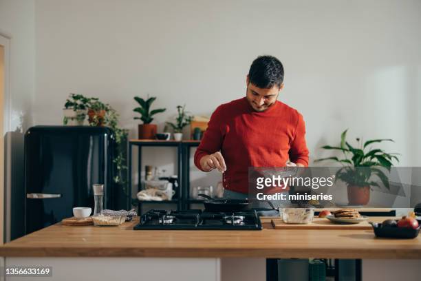 hombre guapo y alegre de pie en una cocina preparando una comida - cook fotografías e imágenes de stock
