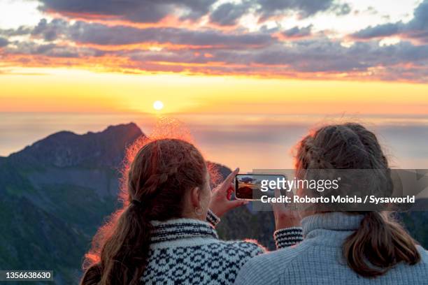 personal perspective of women photographing sunset with smartphone, norway - senja stockfoto's en -beelden