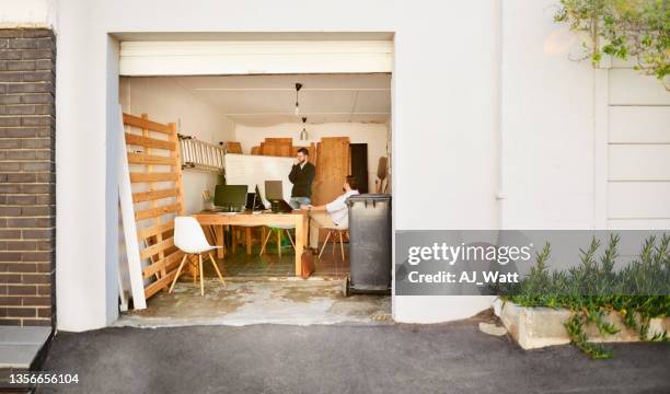 two young men working inside of a garage on their startup - carport stockfoto's en -beelden