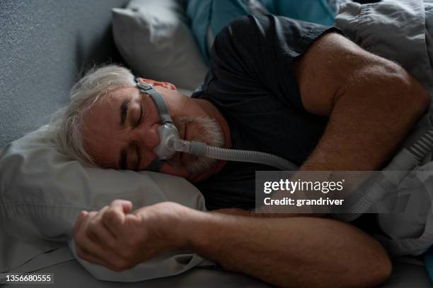 mature man with sleep apnea wearing a cpap mask in bed sleeping - sleep apnea stock pictures, royalty-free photos & images