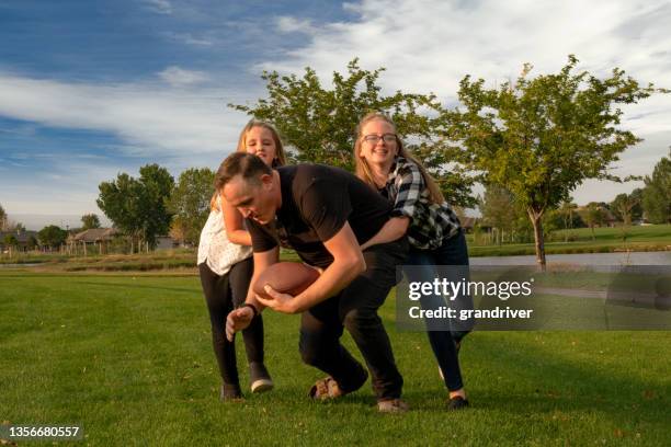 young father playing touch football with his two daughters on a grassy field in a park late afternoon summertime - afl players stock pictures, royalty-free photos & images