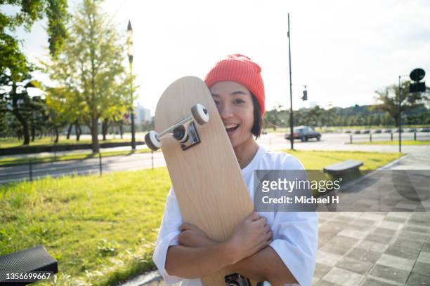 a portrait of a woman hugging a skateboard and laughing. - alternative lifestyle stock pictures, royalty-free photos & images