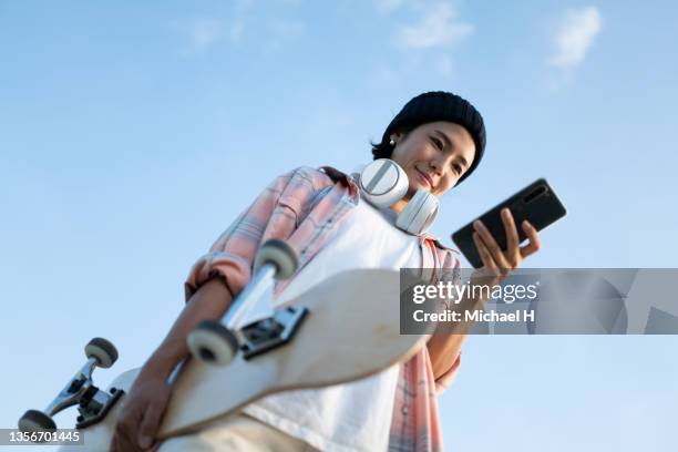 a female skateboarder standing against the blue sky. - longboard skating stock pictures, royalty-free photos & images