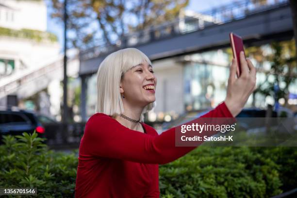 junge frau mit platinblonder perücke und rotem hemd beim selfie-foto auf der straße - frau blond perücke stock-fotos und bilder