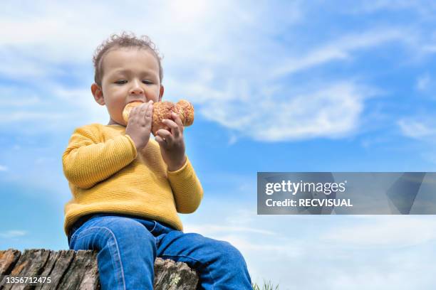 boy eating croissant outdoors in the park - parte del cuerpo humano stock pictures, royalty-free photos & images