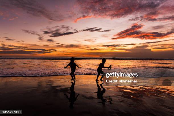 silhouette of small kids having fun on the beach at sunset. - child silhouette ocean stock pictures, royalty-free photos & images