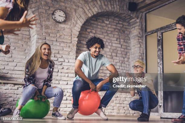 joyful friends having fun during hoppity horse game at casual office. - space hopper stock pictures, royalty-free photos & images