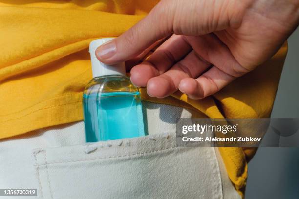 a woman's hand takes out or puts a bottle of disinfectant gel, alcohol, sanitizer in the back pocket of jeans, against the background of bright clothes. prevention of pandemics, colds and flu. preventing the spread of coronavirus and covid-19. - back pocket stock pictures, royalty-free photos & images