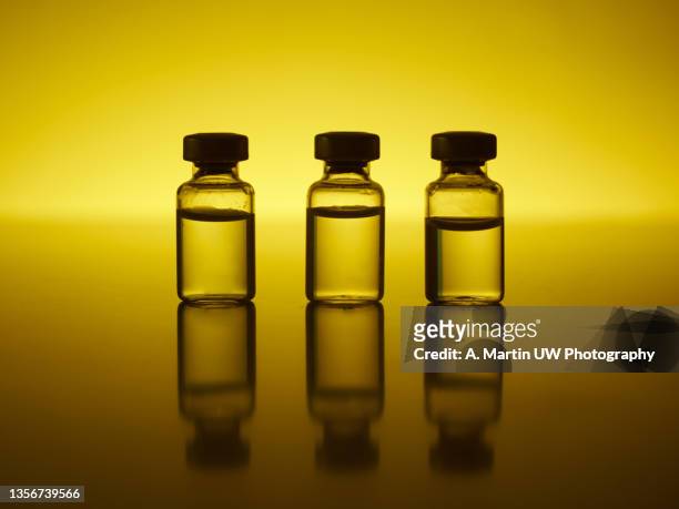 three coronavirus vaccine vials on a table with reflections and backlighting - 3 shot fotografías e imágenes de stock