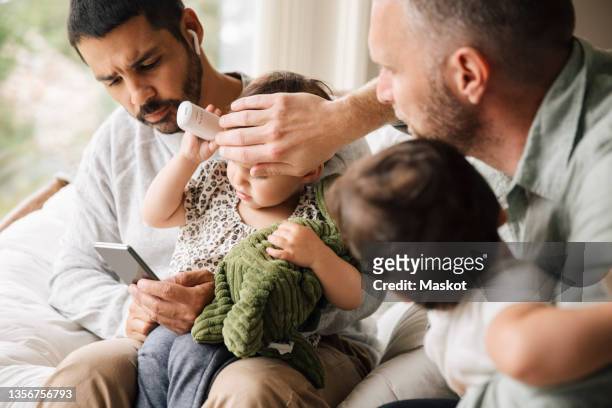father checking temperature of daughter while boyfriend taking advice on video call - stockholm syndrome stock pictures, royalty-free photos & images