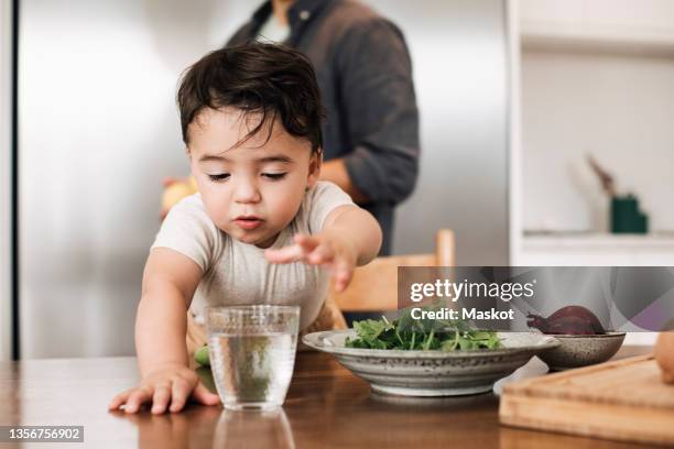 baby boy looking at drinking glass in kitchen - familly glasses stockfoto's en -beelden