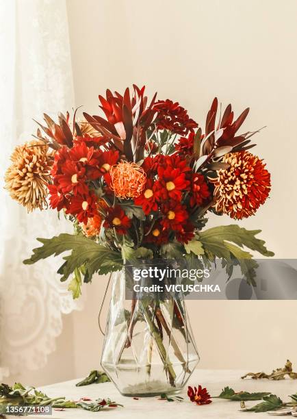 beautiful red flower bouquet with chrysanthemum, lilies and gerbera in glass vase at beige wall background - bouquet of chrysanthemums stock pictures, royalty-free photos & images