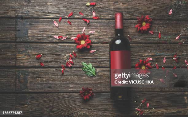red wine bottle with empty red label mock up on rustic wooden kitchen table with red flower petals - wein etikette stock-fotos und bilder